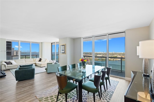 dining area with light wood-type flooring, a healthy amount of sunlight, expansive windows, and a water view