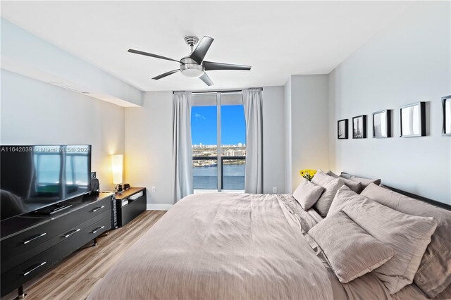 bedroom featuring light hardwood / wood-style floors, ceiling fan, a water view, and access to outside