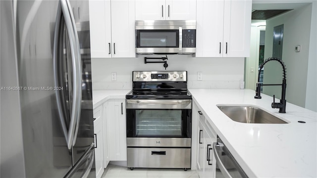 kitchen with white cabinetry, appliances with stainless steel finishes, sink, and light stone countertops