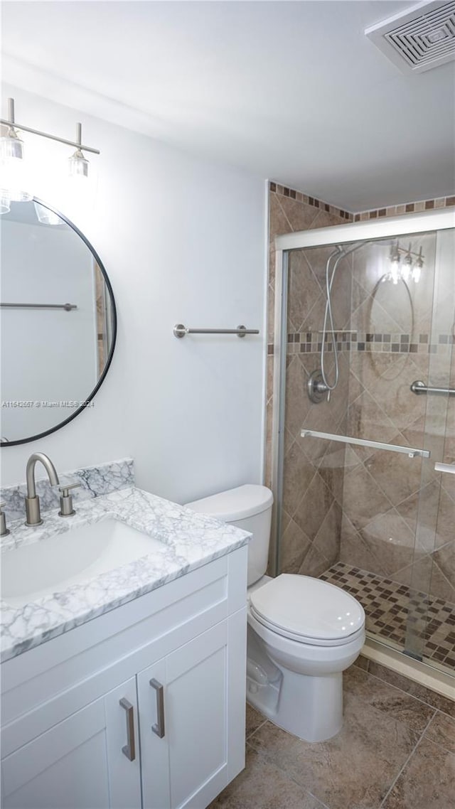 bathroom with tile patterned flooring, a shower with door, vanity, and toilet