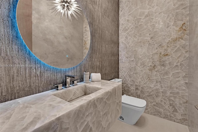 bathroom with toilet, an inviting chandelier, tile walls, and sink