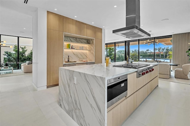 kitchen with island range hood, light stone counters, stainless steel appliances, an inviting chandelier, and a center island