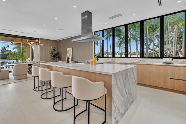 kitchen featuring light stone countertops, island range hood, a large island, and sink