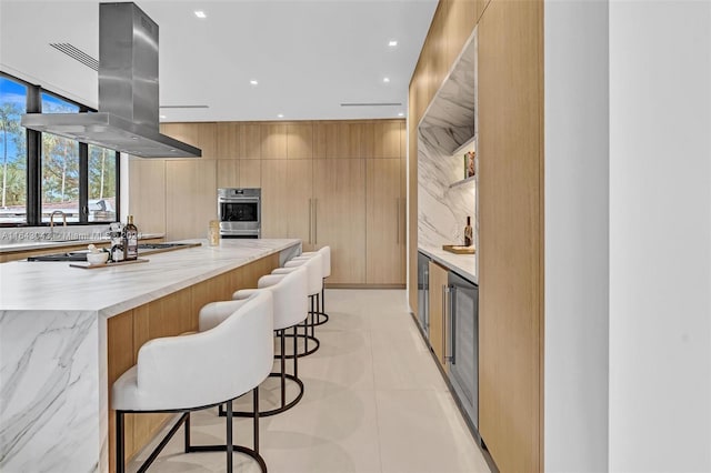 kitchen featuring light tile patterned floors, tasteful backsplash, a large island, a kitchen breakfast bar, and island exhaust hood