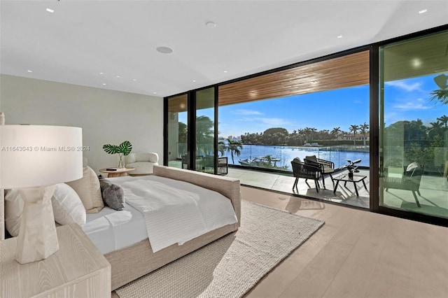 bedroom with access to exterior, hardwood / wood-style floors, a wall of windows, and a water view