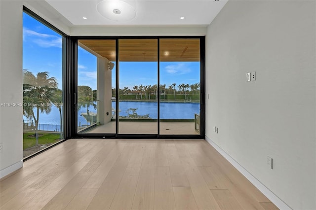 empty room featuring light wood-type flooring, a water view, and floor to ceiling windows