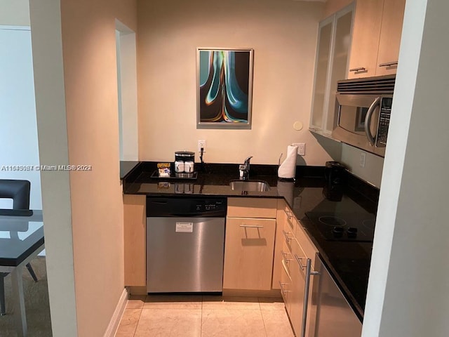 kitchen with appliances with stainless steel finishes, light tile patterned flooring, dark stone countertops, and sink