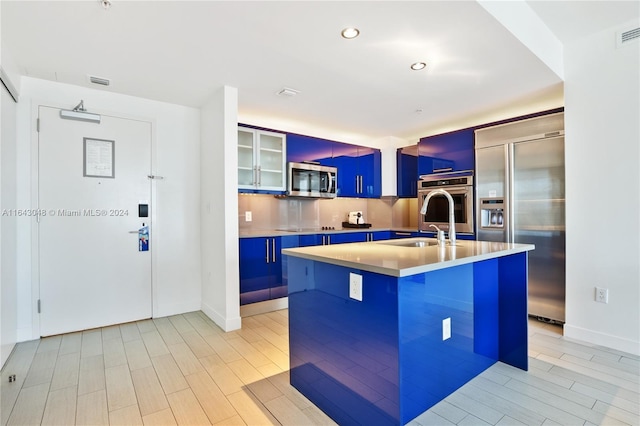 kitchen featuring blue cabinets, decorative backsplash, and an island with sink