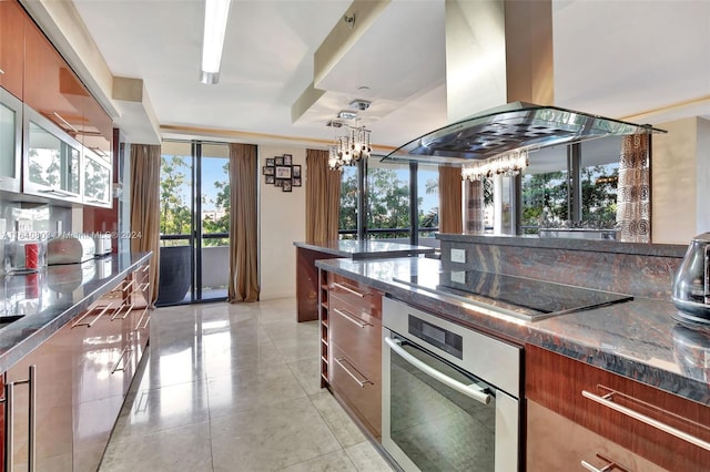 19667 Turnberry Way Unit 3E, Aventura, FL 33180 - kitchen featuring dark stone counters, an inviting chandelier, island exhaust hood, black electric cooktop, and oven