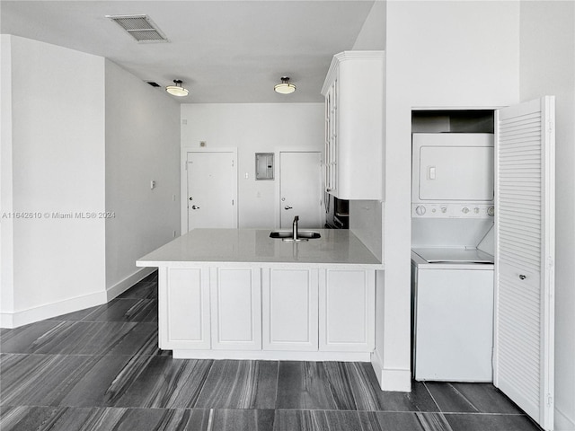 kitchen with kitchen peninsula, white cabinetry, stacked washing maching and dryer, and dark tile patterned floors