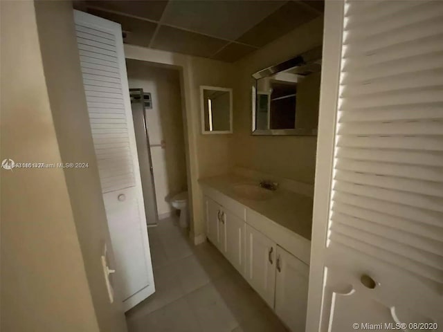 bathroom with tile patterned flooring, toilet, a drop ceiling, and vanity