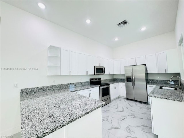 kitchen with kitchen peninsula, appliances with stainless steel finishes, sink, stone counters, and white cabinetry