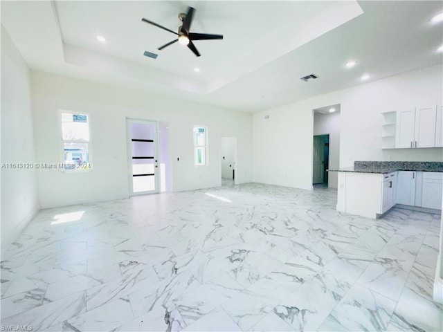 unfurnished living room featuring a tray ceiling and ceiling fan