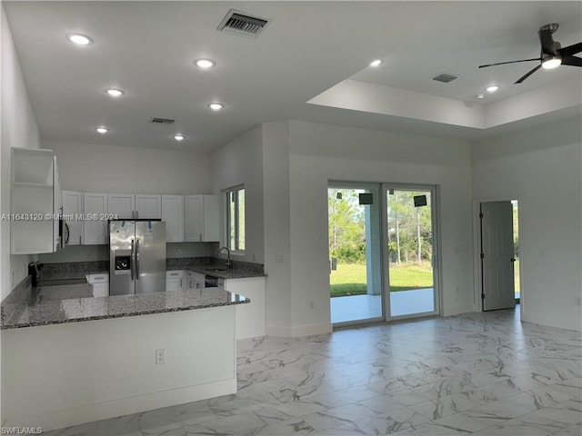 kitchen with stone counters, sink, stainless steel refrigerator with ice dispenser, kitchen peninsula, and white cabinets