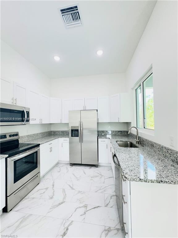 kitchen featuring light stone countertops, appliances with stainless steel finishes, white cabinetry, and sink