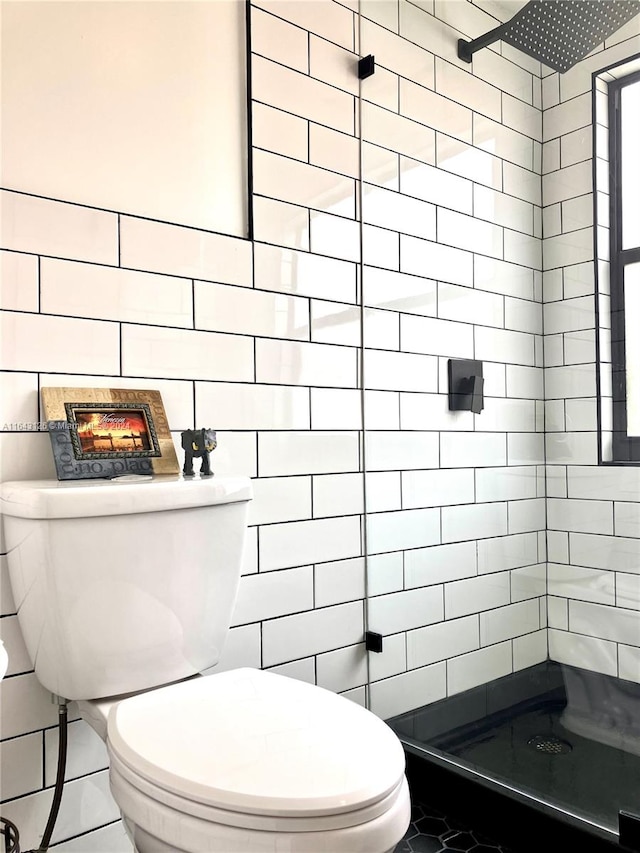 bathroom with a tile shower, toilet, tile patterned floors, and tile walls