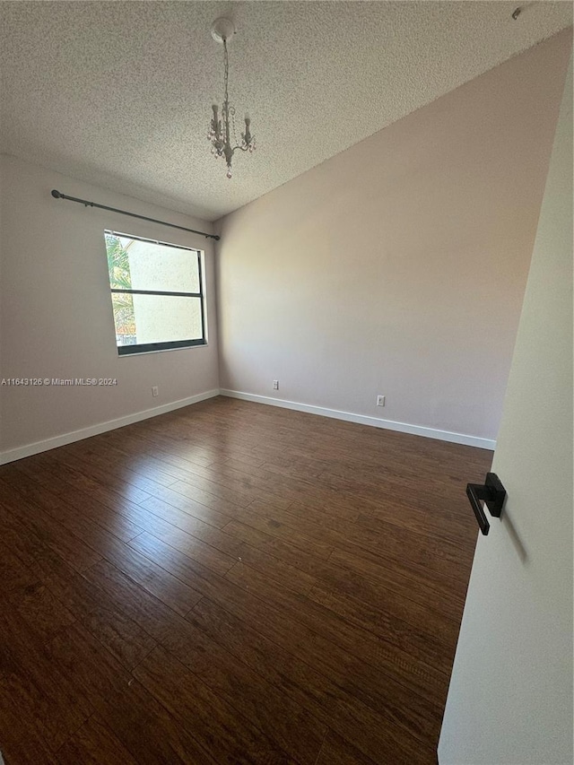 spare room featuring a textured ceiling, a notable chandelier, and dark hardwood / wood-style floors