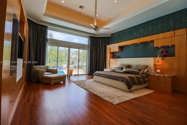 bedroom with a high ceiling, visible vents, a raised ceiling, and wood finished floors