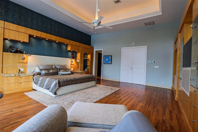 bedroom featuring wood finished floors, a raised ceiling, visible vents, and baseboards