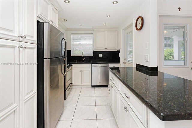 kitchen featuring stainless steel appliances, crown molding, light tile patterned flooring, and dark stone counters