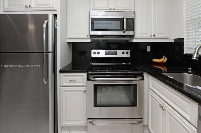 kitchen with sink, backsplash, stainless steel appliances, white cabinets, and dark stone counters