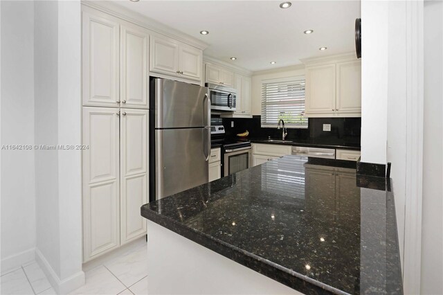 kitchen with dark stone countertops, appliances with stainless steel finishes, decorative backsplash, light tile patterned floors, and kitchen peninsula