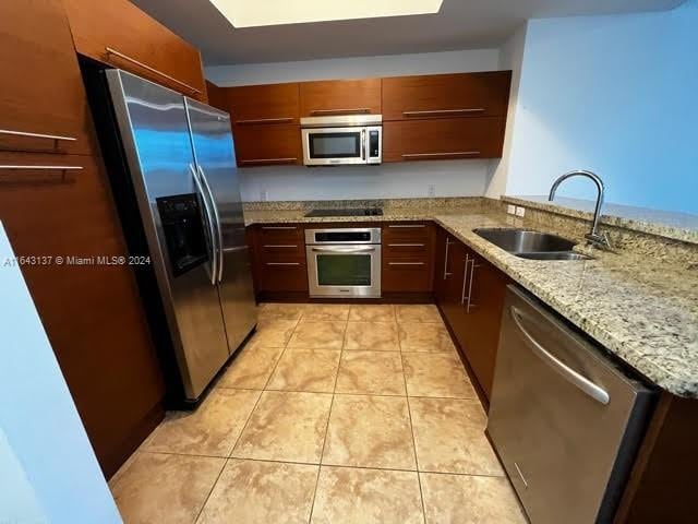 kitchen featuring appliances with stainless steel finishes, sink, light stone countertops, light tile patterned floors, and kitchen peninsula