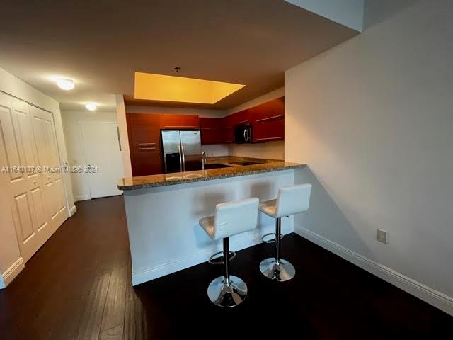 kitchen featuring appliances with stainless steel finishes, stone counters, dark hardwood / wood-style floors, and kitchen peninsula