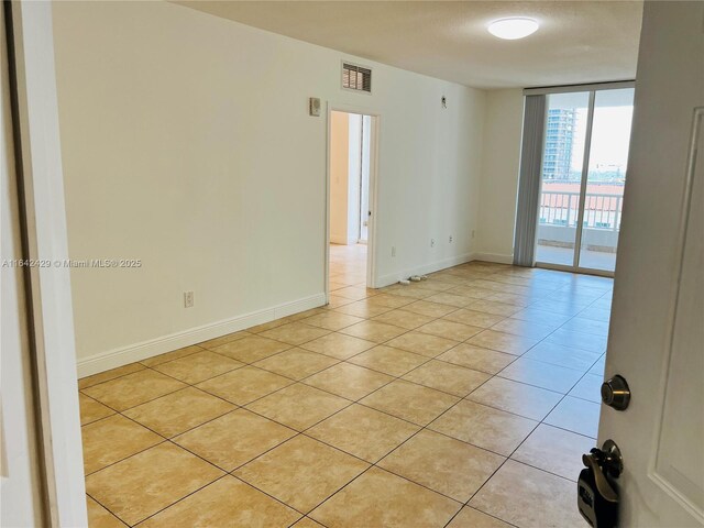 unfurnished room with floor to ceiling windows, light tile patterned floors, and a textured ceiling