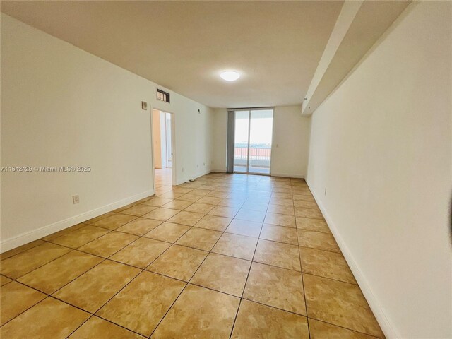 empty room with light tile patterned flooring and a wall of windows