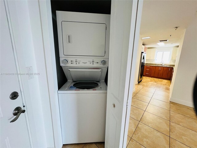 clothes washing area featuring light tile patterned floors, stacked washer and clothes dryer, and sink