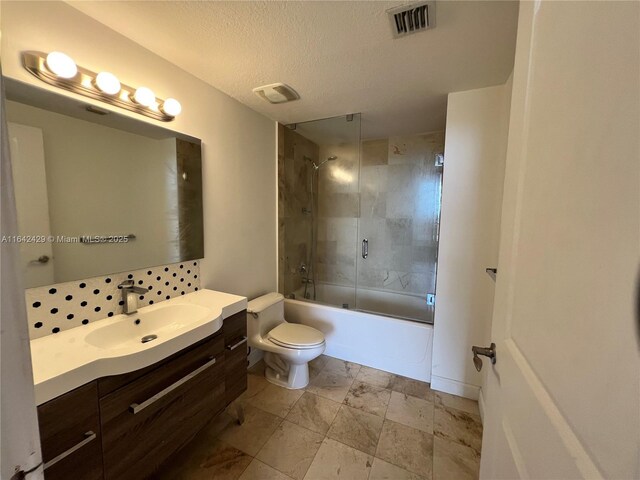 full bathroom featuring shower / bath combination with glass door, vanity, a textured ceiling, and toilet