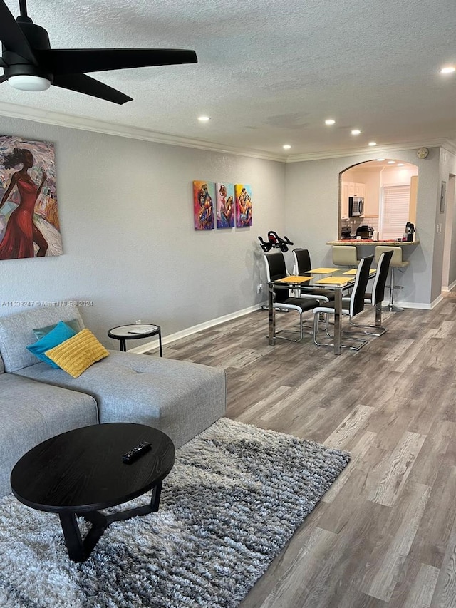 living room featuring ceiling fan, crown molding, wood-type flooring, and a textured ceiling