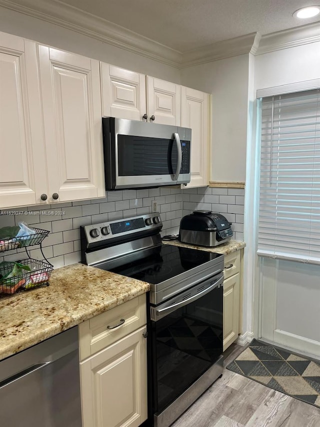 kitchen with crown molding, appliances with stainless steel finishes, light stone countertops, light hardwood / wood-style floors, and backsplash