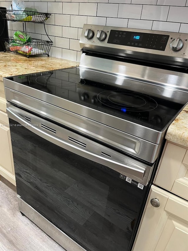 kitchen with tasteful backsplash, light wood-type flooring, light stone countertops, and stainless steel electric range oven