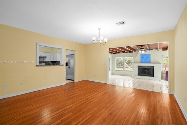 unfurnished living room featuring lofted ceiling with beams, light hardwood / wood-style floors, and ceiling fan with notable chandelier