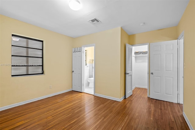 unfurnished bedroom with wood-type flooring, ensuite bathroom, and a closet