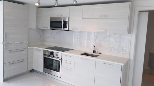 kitchen with appliances with stainless steel finishes, white cabinetry, sink, decorative backsplash, and track lighting