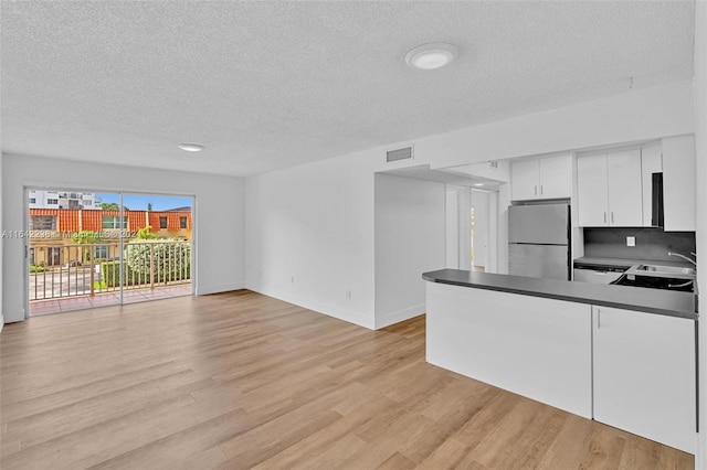 kitchen featuring sink, stainless steel refrigerator, light hardwood / wood-style floors, a textured ceiling, and white cabinets