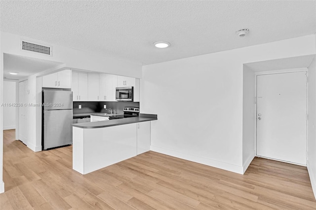 kitchen with white cabinets, light hardwood / wood-style floors, kitchen peninsula, stainless steel appliances, and a textured ceiling