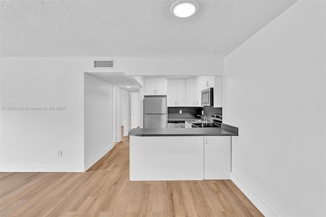 kitchen with appliances with stainless steel finishes, white cabinetry, sink, light hardwood / wood-style floors, and kitchen peninsula