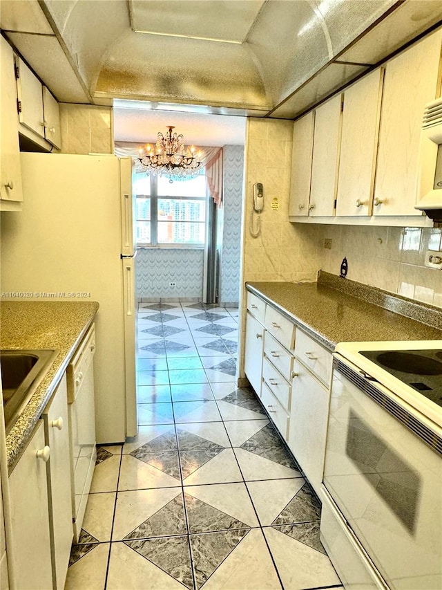 kitchen with decorative backsplash, an inviting chandelier, white cabinets, light tile patterned floors, and white appliances