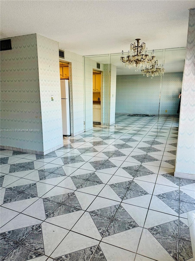 tiled spare room featuring a textured ceiling and a chandelier