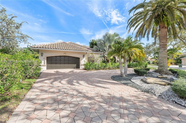 view of front of property featuring a tile roof, decorative driveway, a garage, and stucco siding