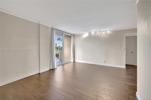 empty room featuring a textured ceiling, expansive windows, rail lighting, and hardwood / wood-style flooring