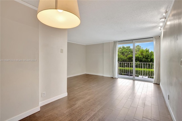 unfurnished room featuring a textured ceiling, floor to ceiling windows, rail lighting, and hardwood / wood-style flooring