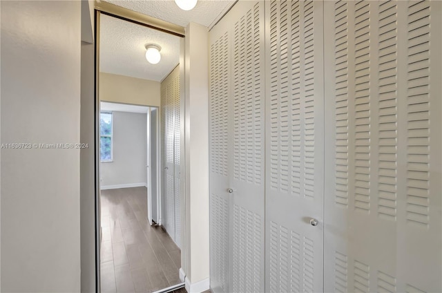 hallway with a textured ceiling and wood-type flooring