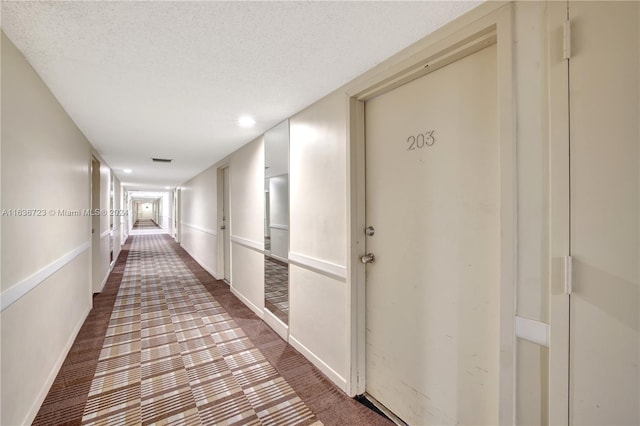 hall with dark carpet and a textured ceiling