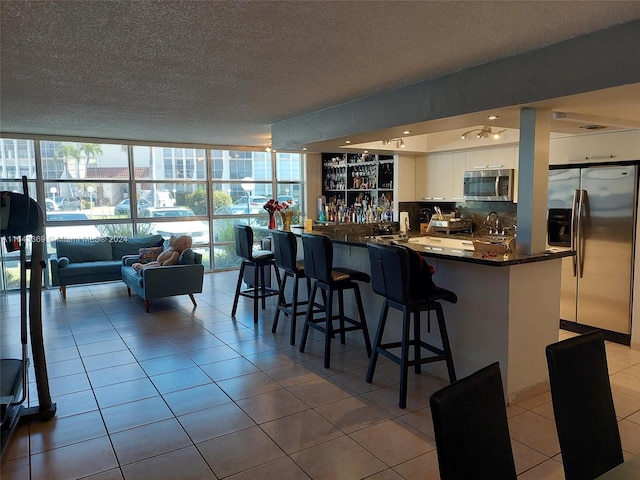 kitchen featuring appliances with stainless steel finishes, white cabinetry, kitchen peninsula, light tile patterned flooring, and decorative backsplash