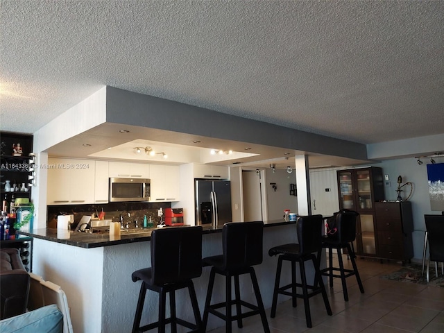 kitchen with white cabinets, appliances with stainless steel finishes, kitchen peninsula, tasteful backsplash, and a textured ceiling